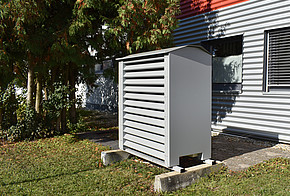 Luftwärmepumpe mit Einhausung vor einem Haus