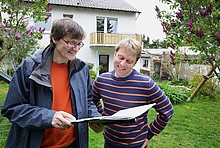 Energieberater mit Mappe voller Unterlagen und Kunde im Gespräch im Garten eines Wohngebäudes